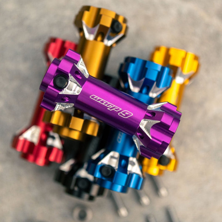 Stack of Warp 9 jackshafts in multiple colors, featuring purple, blue, red, gold, and black finishes